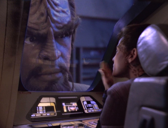 A still from "One Little Ship" featuring Worf looking through the window of a tiny runabout, with Jadzia inside blowing him a kiss.