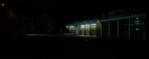 Night scene: an empty, somewhat run-down looking car wash that looks just a little dystopian. Faint streetlights further away in the picture.
