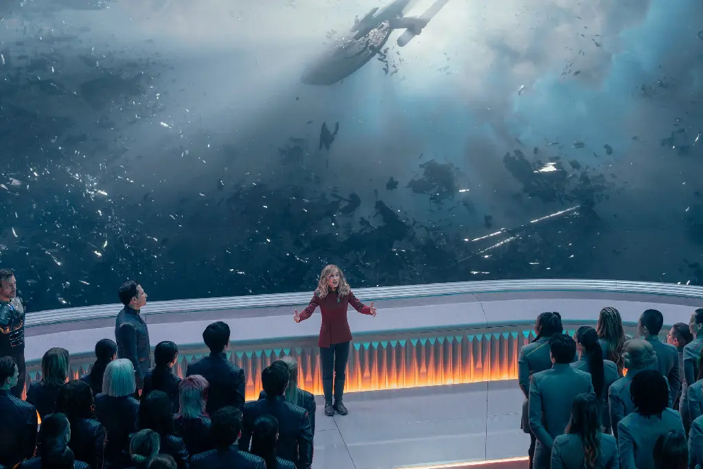 Nahla Ake addressing cadets in front of a window. Outside, you can see a derelict Starfleet ship.